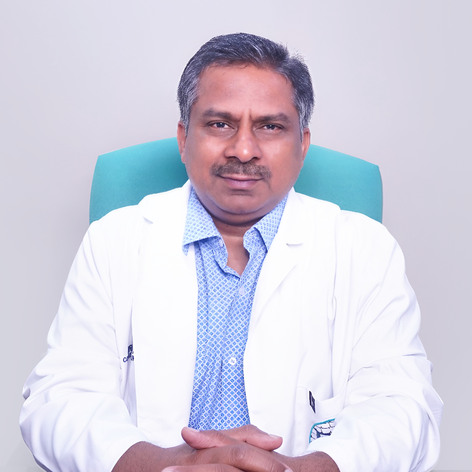 Portrait of Dr. G. Srihari, a male neurosurgeon wearing a white coat and stethoscope, smiling, vertical rectangle photo